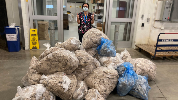 a staff member showing thumbs up, standing behind a mound of bags full of paper towels