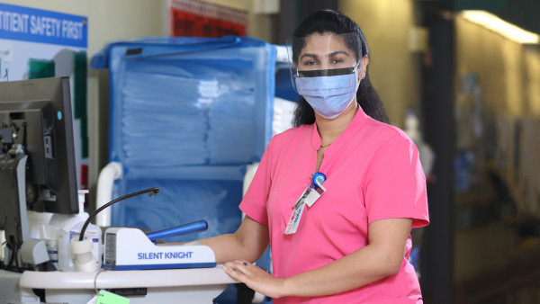 Jasmine Devassy wearing a pink nurses top, standing by a monitor at Parkwood Institute