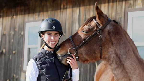 Grace Hicks holding her horse Nova by the bridle as it nuzzles her shoulder