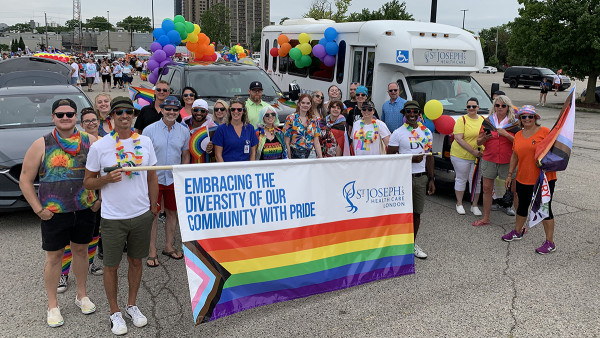 a large group of parade participants wearing clothes with the pride stripes holding a pride-themed sign that reads "Embracing the diversity of our community with pride."