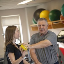 A person stretching arm out holding a weight receiving assistance by another person