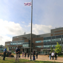 Wampum flag flying high atop the flagpole with ceremony participants looking up at it.