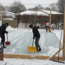 Three people clearing snow off an ice rink