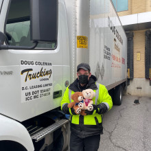 man holds up a teddy bear next to 18-wheel truck
