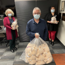 a man holds a bag of teddy bears with two women behind him