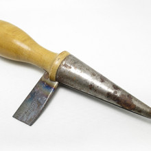 A tool with a wooden handle and broken metal blade extending from the side of the handle and a conical metal end