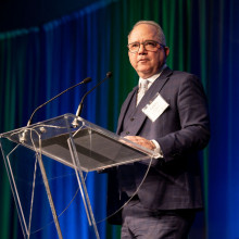 A man (Roy Butler) standing on stage at a podium