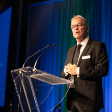 A man (Bill Tucker) standing on stage at a podium