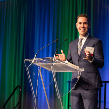 A man (Will Heeman) standing on stage at a podium