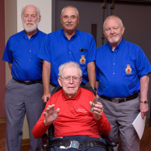 three men in blue stand behind a veteran in a wheelchair