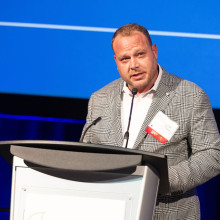 Adam Tyman speaking at a podium