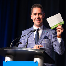 Man speaking at podium holding up card