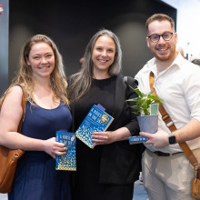 Two woman and one man posing with book and plant