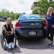 Sarah King and Jenny Iszakovits, OT, pose outside a specialized car used for rehabilitation