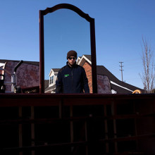 A man is looking into a mirror as he is moving several items of furniture
