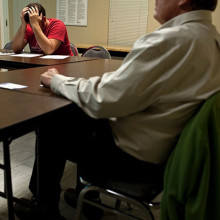 A young man with his head in his hands sitting at a table with another person