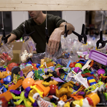 A pile of toys and a man placing them in plastic bags